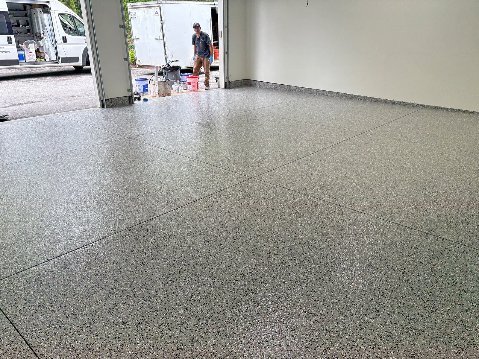 Light grey flake epoxy and polyaspartic garage floor filling the frame, photographed from inside the garage with the door open